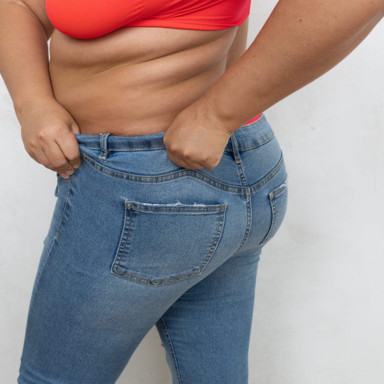 Cropped rearview of overweight, fat female with cellulite friable body try to get dressed and fit in small size jeans on white background. Successful attempt burn calories and rid of fat. Copy space